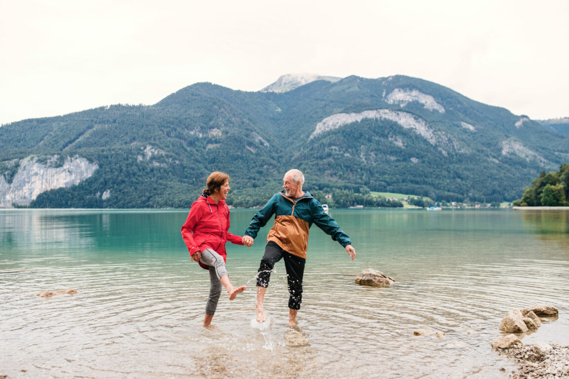 Older couple holding hands in water with mountains in background